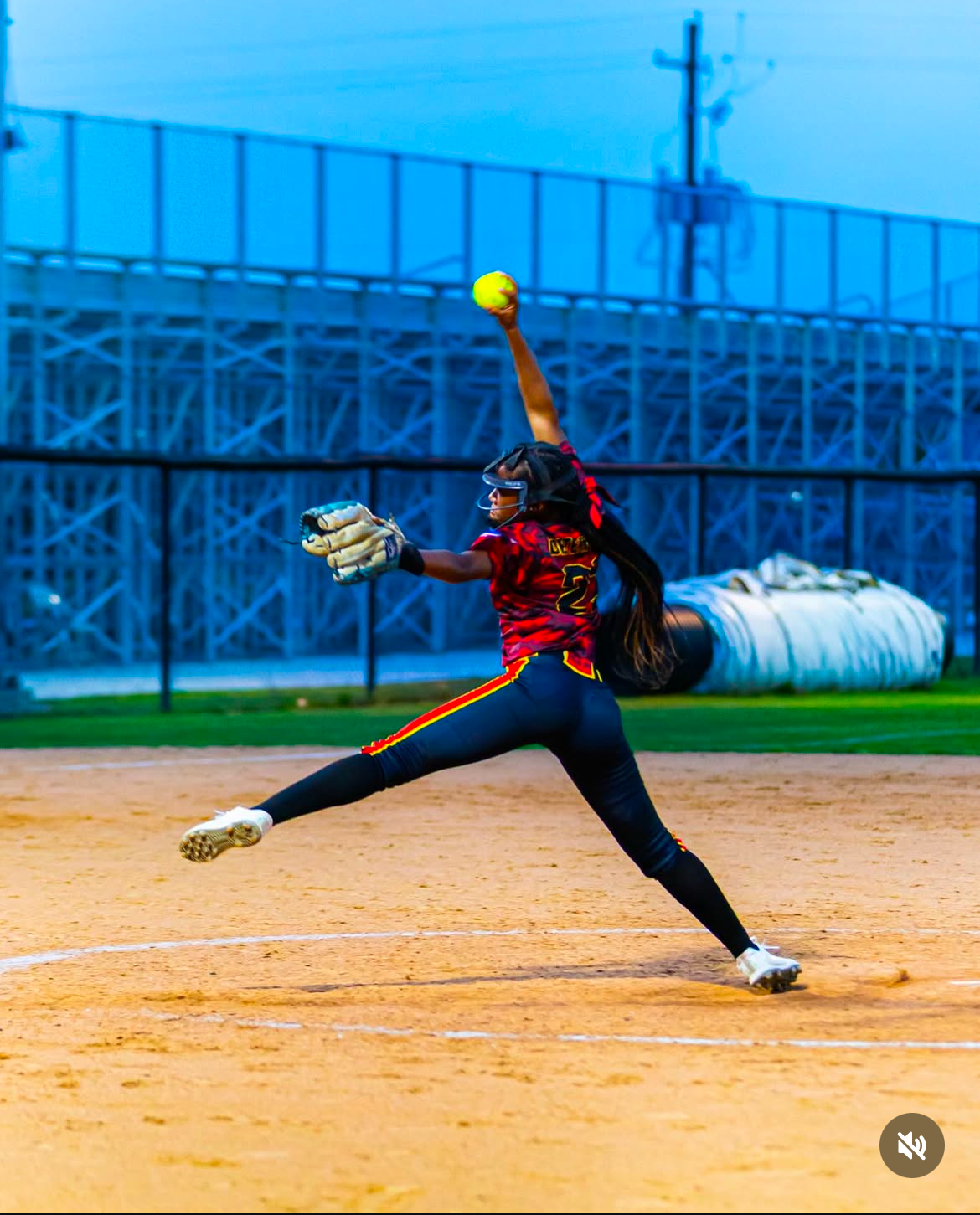 Skye Hebert exploding toward home in her pitching motion at dusk